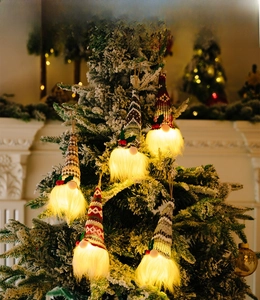 Set of five glowing Christmas gnomes with warm LED lights hanging on a festive tree