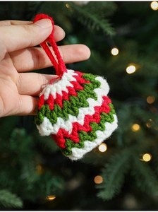 Detail of a handmade knit Christmas ornament held by hand with warm festive lights