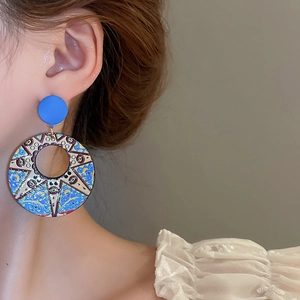 Close-up of artistic blue enamel round drop earrings worn by a model in warm light