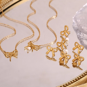 Elegant gold bow jewelry set with pearls and heart charms on a mirrored tray