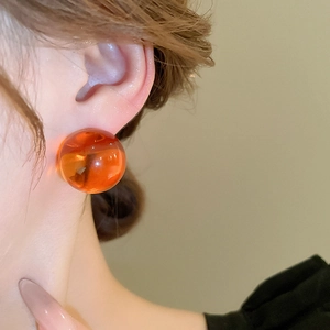 Gros plan de boucles d'oreilles boules en résine ambre translucide sur un modèle