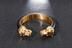 Detail of dual golden lion heads on a black leather-textured open cuff bracelet