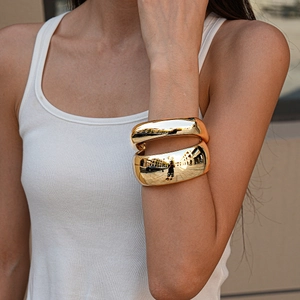 Close-up of stacked chunky gold acrylic geometric bracelets with a mirror polished finish