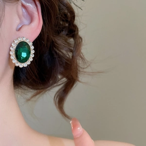 Close-up of vintage gold earrings featuring oval green gemstones and crystal halos