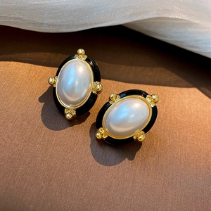 Close-up of vintage oval earrings with golden metal, white faux pearl and black enamel detail
