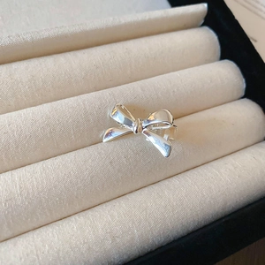 Close-up of a mini silver metal bow hair clip on a beige textured jewelry display box