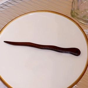 Detail of a wavy dark reddish-brown wooden hair pin on a white ceramic plate