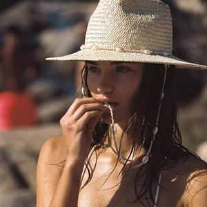 Detailed close-up of a straw hat with a shell chain and woven texture on a beach