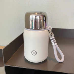 Detail of matte cream insulated flask featuring a silver metal cap and woven wrist strap