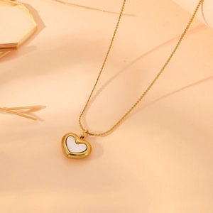 Macro detail of a golden heart necklace with white shell inlay against warm tones