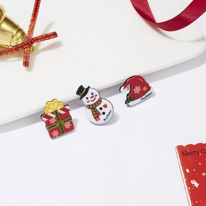 Detailansicht von Schneemann- und Geschenk-Emaille-Pins auf einem weißen Weihnachtsteller
