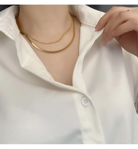 Detail of layered gold double snake and bead chain necklace on a white shirt