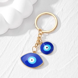 Golden keychain featuring blue enamel evil eye charms on a textured white background