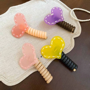 Détail de quatre pinces à cheveux spirales en forme de cœur sur un tissu beige texturé
