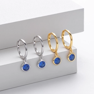Close-up of gold and silver S925 sterling silver hoops with round blue gemstone pendants
