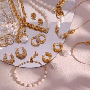 Detailed close-up of luxury gold-plated jewelry set with elegant pearls on reflective glass