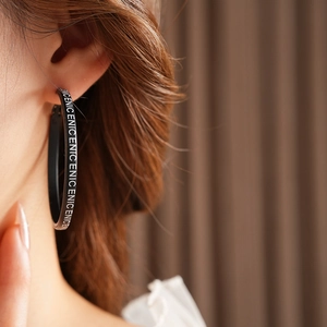 Gros plan de boucles d'oreilles créoles noires avec lettrage NICE blanc sur modèle