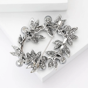 Detail of silver wreath brooch with grey pearls on white cubes with soft lighting