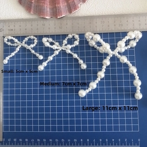 Three sizes of white pearl bow accessories with measurements on a blue cutting mat