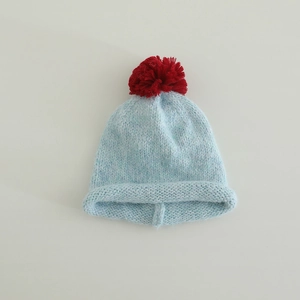 Detail of light blue knit hat with red pom-pom and rolled cuff for children