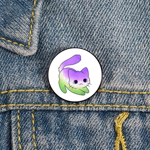 Detailed view of a rainbow gradient glitter cat enamel pin on a denim jacket pocket