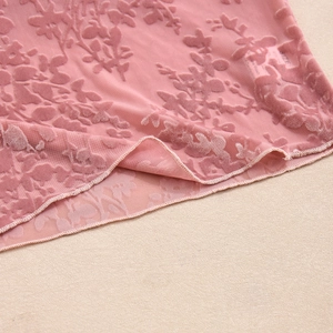 Vue détaillée du tissu en maille floquée rose avec ourlet ondulé et motifs floraux