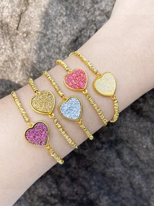 Dettaglio di cinque braccialetti con ciondoli a cuore colorati su sfondo di roccia grigia