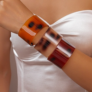 Close-up of three wide tortoise shell resin bangles in amber tones on model's wrist