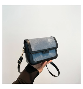 Detail of denim and black leather stitching with golden buckle on the crossbody bag