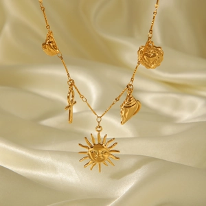 Detail of gold stainless steel necklace with sun and shell charms on silk background