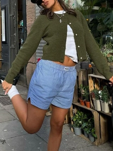 Outdoor street shot of casual green knit cardigan paired with blue striped shorts