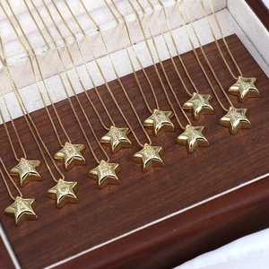 Close-up of gold star pendants with A-L letters inlaid with cubic zirconia on wood tray