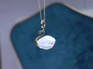 Vue macro du collier cygne avec grande perle baroque blanche et détails dorés