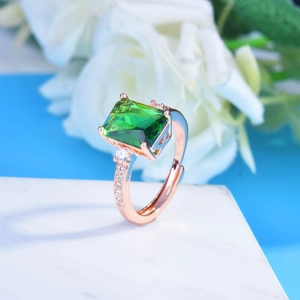Macro shot of rectangular green emerald ring with rose gold band and side diamonds