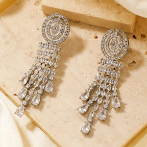 Close-up of silver tassel earrings with zircon inlay on silk background texture