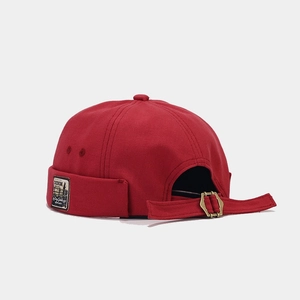 Detail of red canvas docker hat featuring vintage patch and adjustable strap with metal buckle