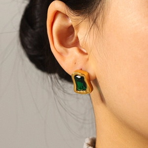 Gros plan d'une boucle d'oreille rétro dorée avec zircon vert émeraude sur un mannequin