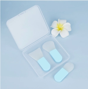 Three silicone face mask brushes with blue handles and storage box on clean background