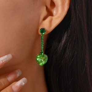 Close-up of elegant gold tassel earrings with green zircon heart pendant on model