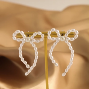 Macro view of French bow earrings with white pearls hanging on a gold luxury display stand