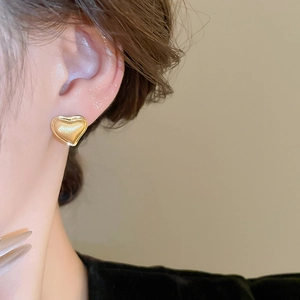 Close-up of minimalist gold heart stud earrings on a model with detailed metal texture