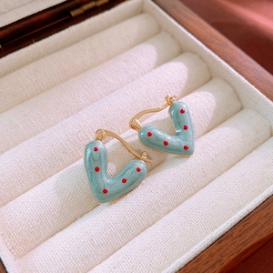 Gros plan de boucles d'oreilles cœur vert menthe à pois rouges dans un écrin en velours beige