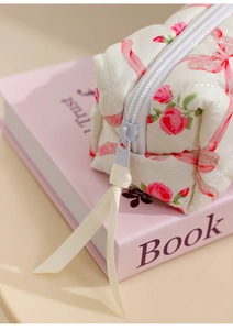 Close-up of beige quilted makeup bag with pink rose patterns and a white ribbon zipper