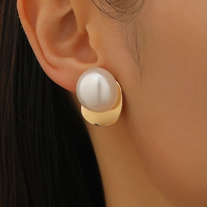 Elegant oversized white pearl stud earrings with a gold metal base on a female model