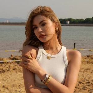 Close-up of golden jewelry set featuring green gemstones worn by model on a sunny beach