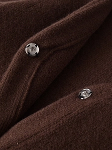 Detailaufnahme von braunem Strickstoff mit Pelzeffekt und silbernem Metalldruckknopf