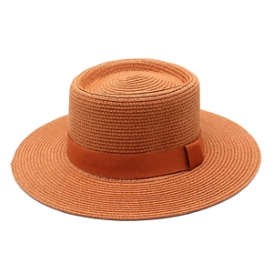 Detailed texture of caramel straw sun hat with flat brim and wide decorative ribbon