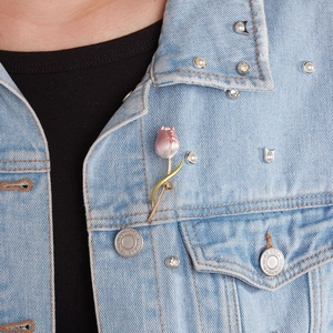 Close-up of a pink enamel tulip brooch pinned on the collar of a blue denim jacket