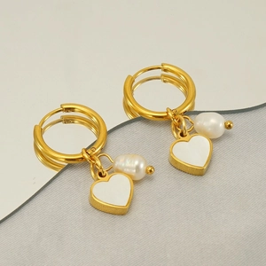 Golden heart and pearl dangle earrings displayed on a reflective mirror surface