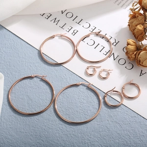 Detailed view of four different sized rose gold stainless steel hoop earrings on blue texture